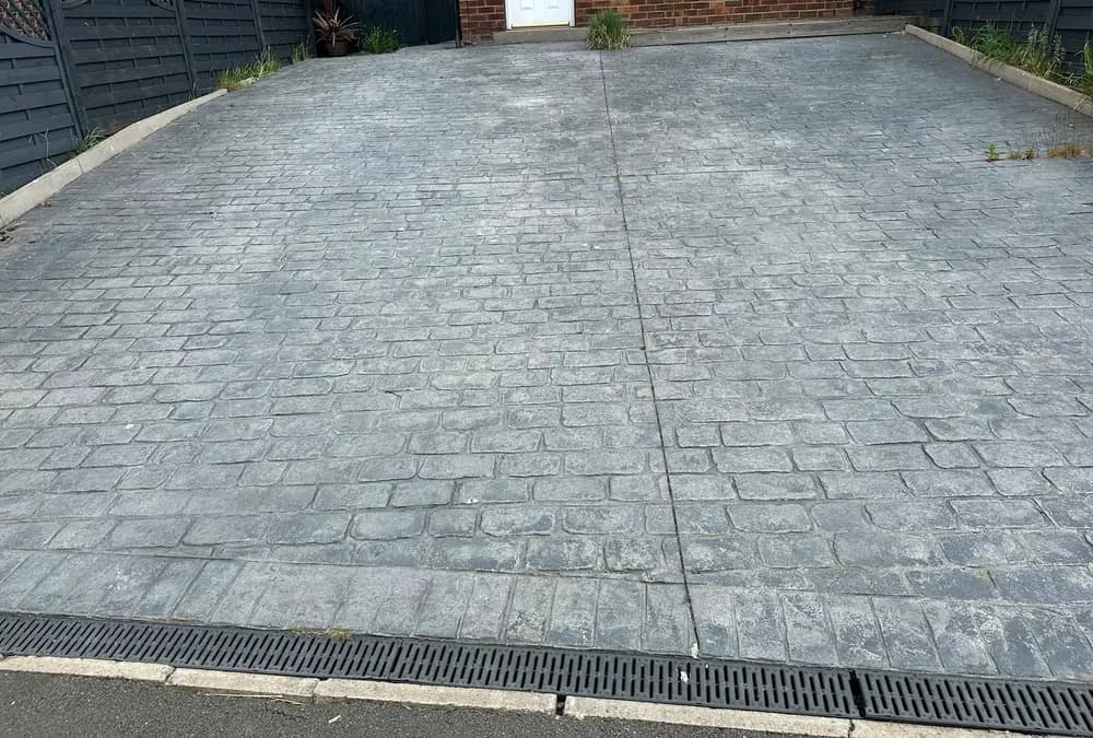 A faded grey imprinted concrete driveway with growth in the joints.