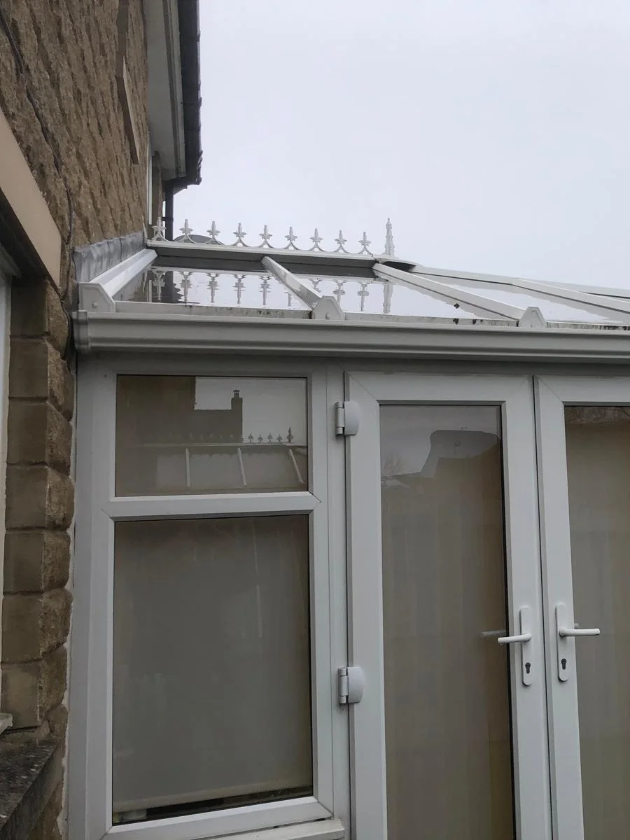 A conservatory built against a stone house wall, its glass roof meeting the wall at a lead lined gutter