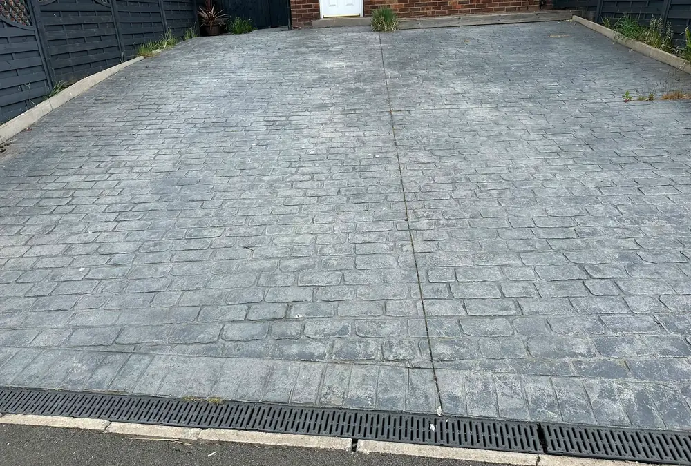 An imprinted concrete drive with a cobble pattern, faded to a flat grey, a straight cut line running down the middle